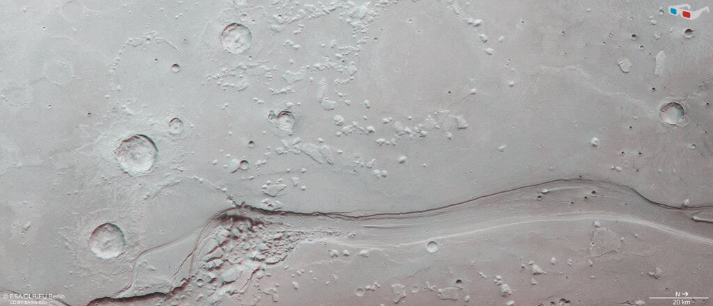 Imagem estereoscópica em tons de cinza da superfície de Marte mostrando um grande canal sinuoso cercado por crateras e formações irregulares. O registro foi preparado para visualização em 3D com óculos vermelho e azul.