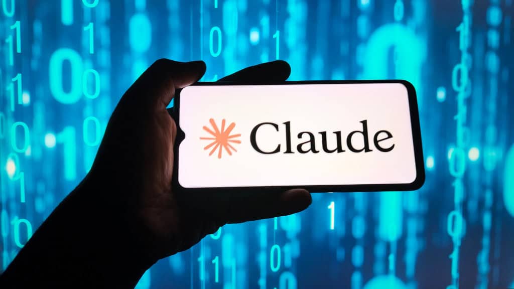 Mão segurando smartphone com o logo do Claude exibido na tela, sobre fundo com números digitais em azul.