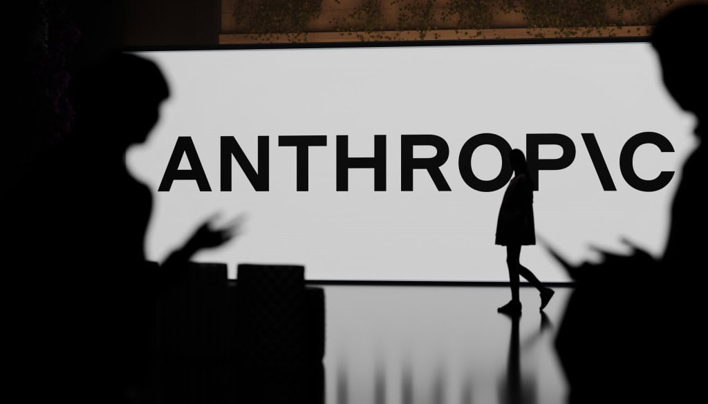 Logo da Anthropic ao fundo, com silhuetas de pessoas passando à frente