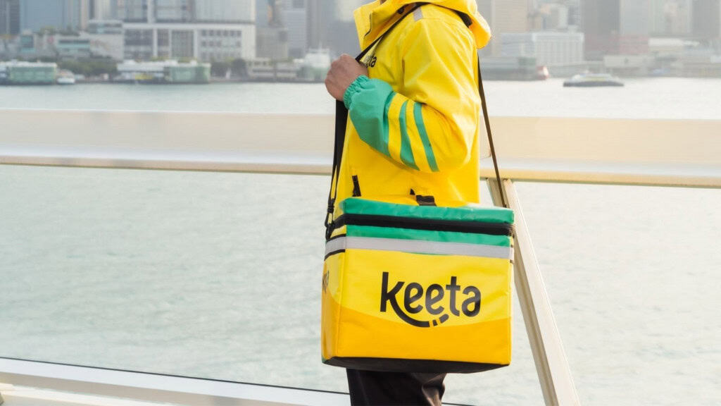 Homem em pé com uniforme e bolsa da Keeta