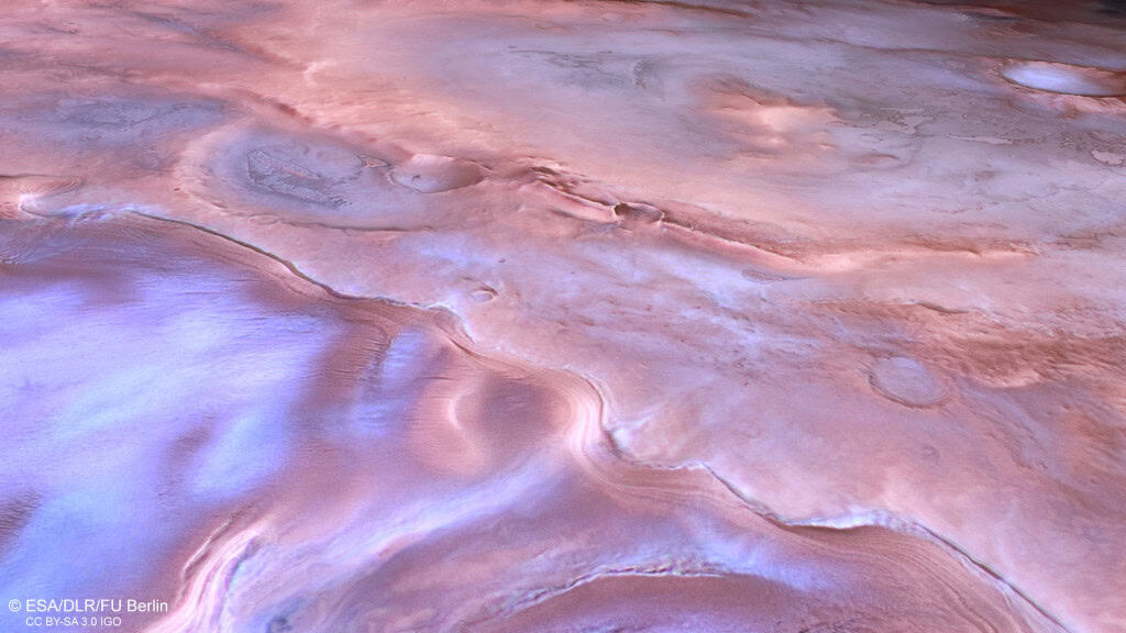 Vista aérea de uma geleira próxima a Thyles Rupes, em Marte, com formações de gelo e terreno em tons de rosa, roxo e branco.