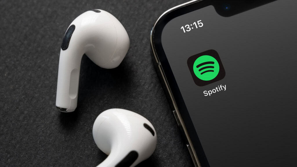 Logo do Spotify em um smartphone, ao lado de um par de fones de ouvido sem fio brancos